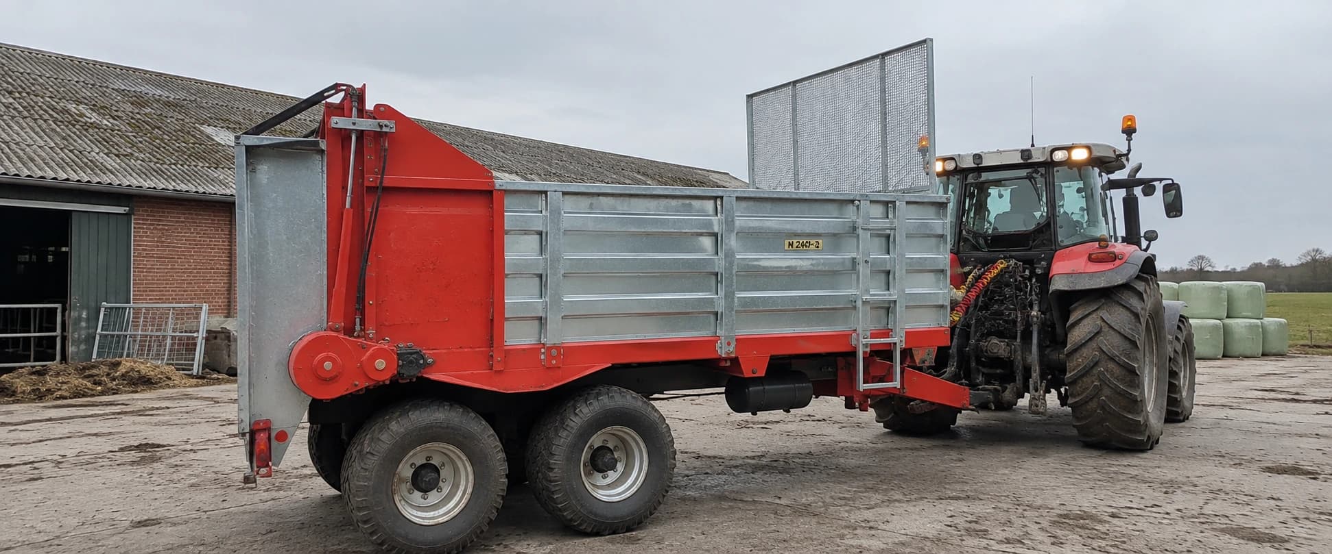 Roter Miststreuer hinter einem Traktor auf einem Hof