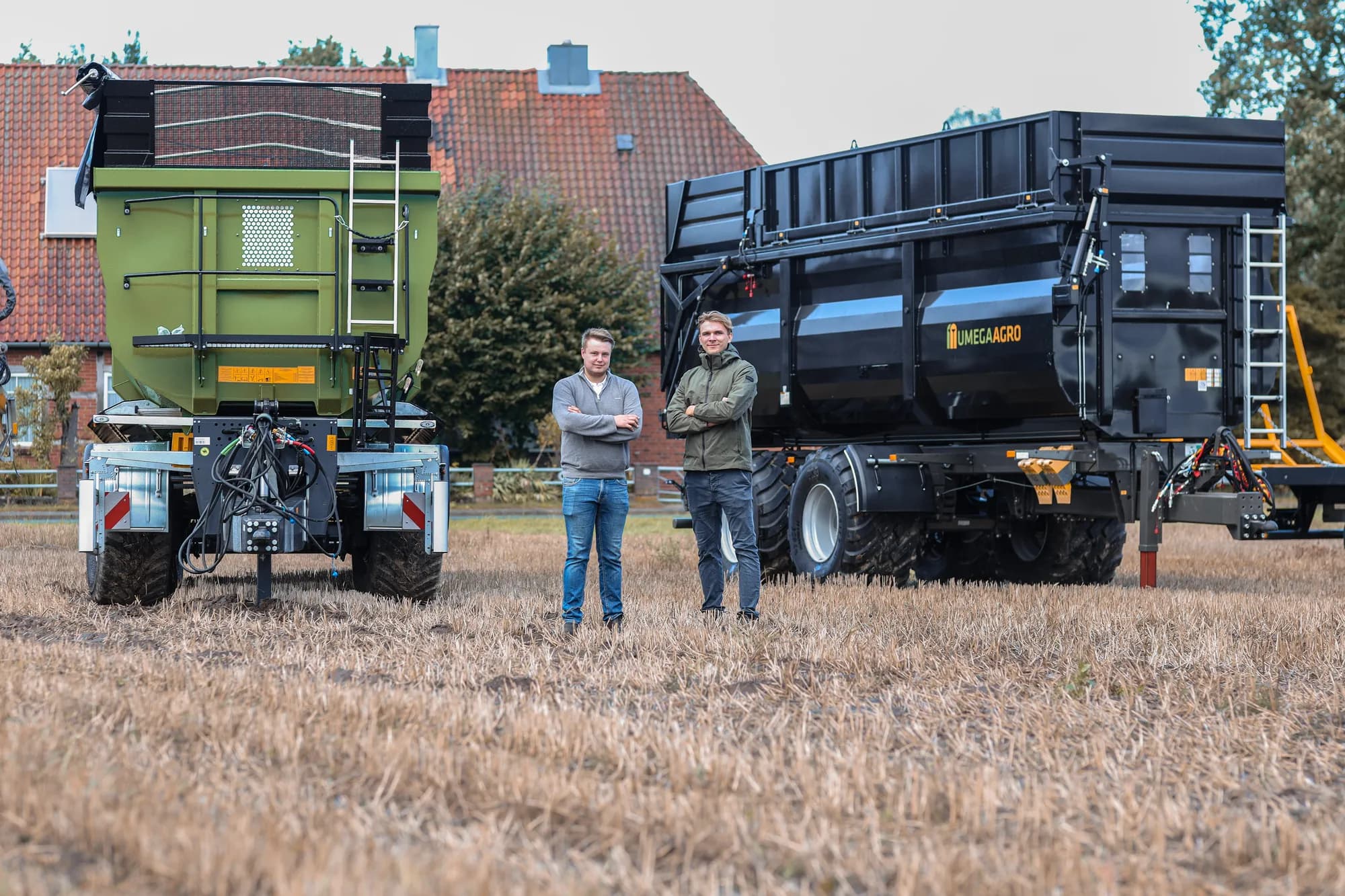 Umega-Anhänger und ein grüner Streuer auf dem Feld vor dem Hofgebäude