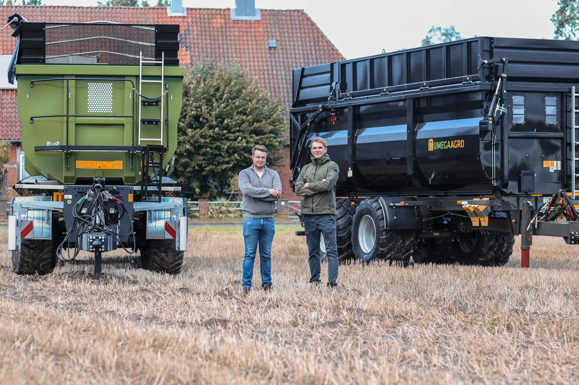 Zwei Männer vor einem grünen Streuer und einem Umega-Agro-Anhänger auf dem Feld